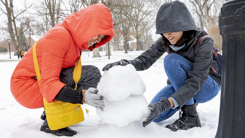 two students in laugh while building a small snowman